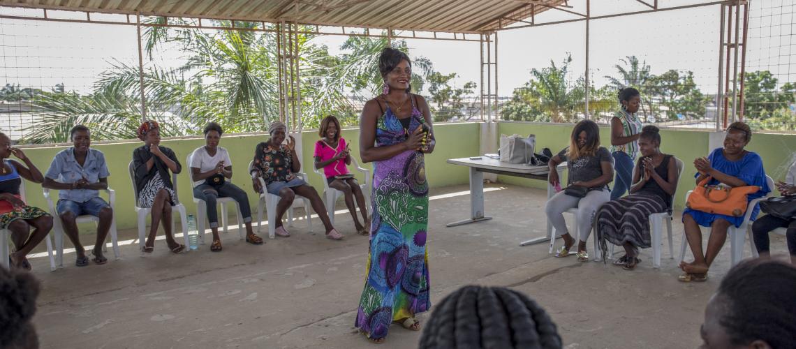 A woman standing in the middle of a goup of people sitting in a gathering