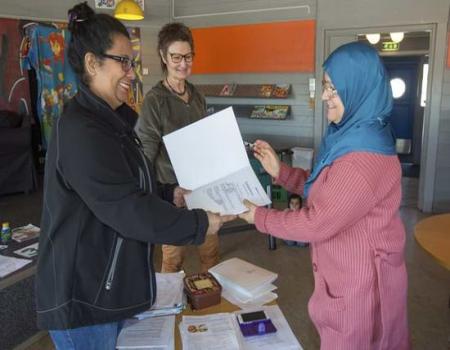 A woman giving paper to another woman in blue burkha